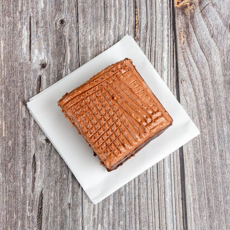 Square chocolate pastry with a textured lattice top on a white plate over rustic wooden boards.
