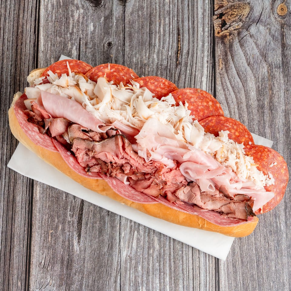 Overhead view of a large Italian sub sandwich layered with salami, ham, roast beef, and shredded chicken on a wooden table.