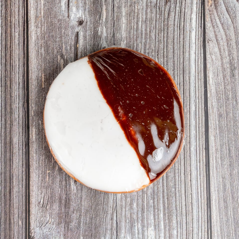 Round pastry topped with white icing and glossy chocolate glaze on a rustic wooden surface.