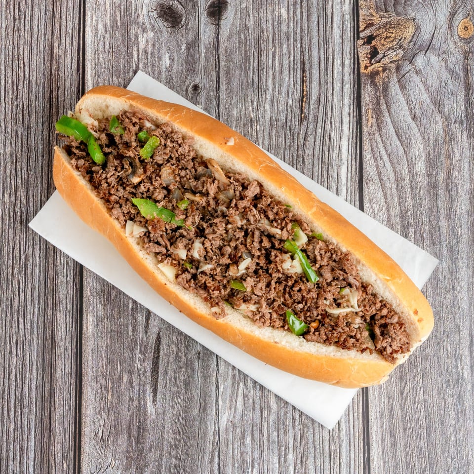Cheesesteak sandwich filled with seasoned chopped beef, melted cheese, green peppers, and onions on a wooden table.