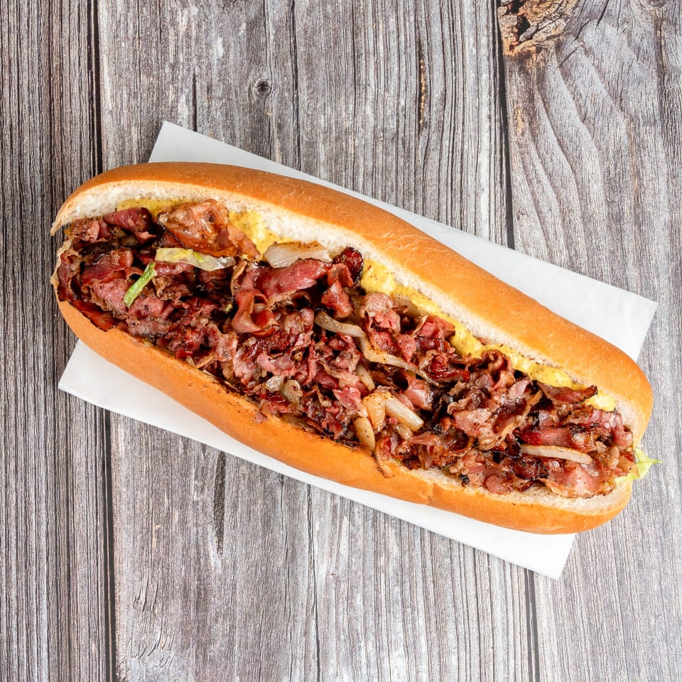 Overhead view of a loaded beef sandwich with grilled onions, lettuce, and mustard on a toasted hoagie roll.